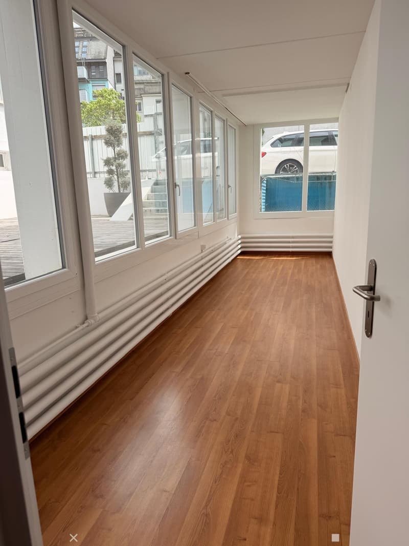 Empty room with wooden flooring, white walls, large windows, and radiators along one wall.