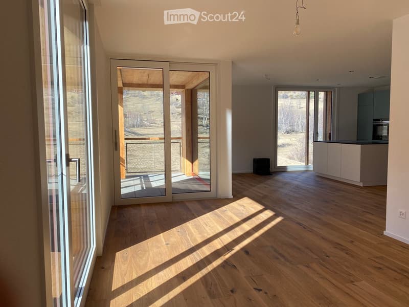Bright, empty room with wooden flooring, large glass doors leading to a balcony, and a view of the outdoors.