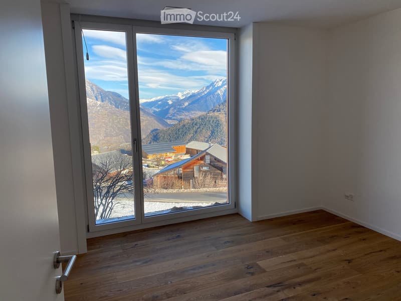 Empty room with wooden flooring, large sliding glass door leading to a scenic mountain view, white walls, and a visible electrical outlet.