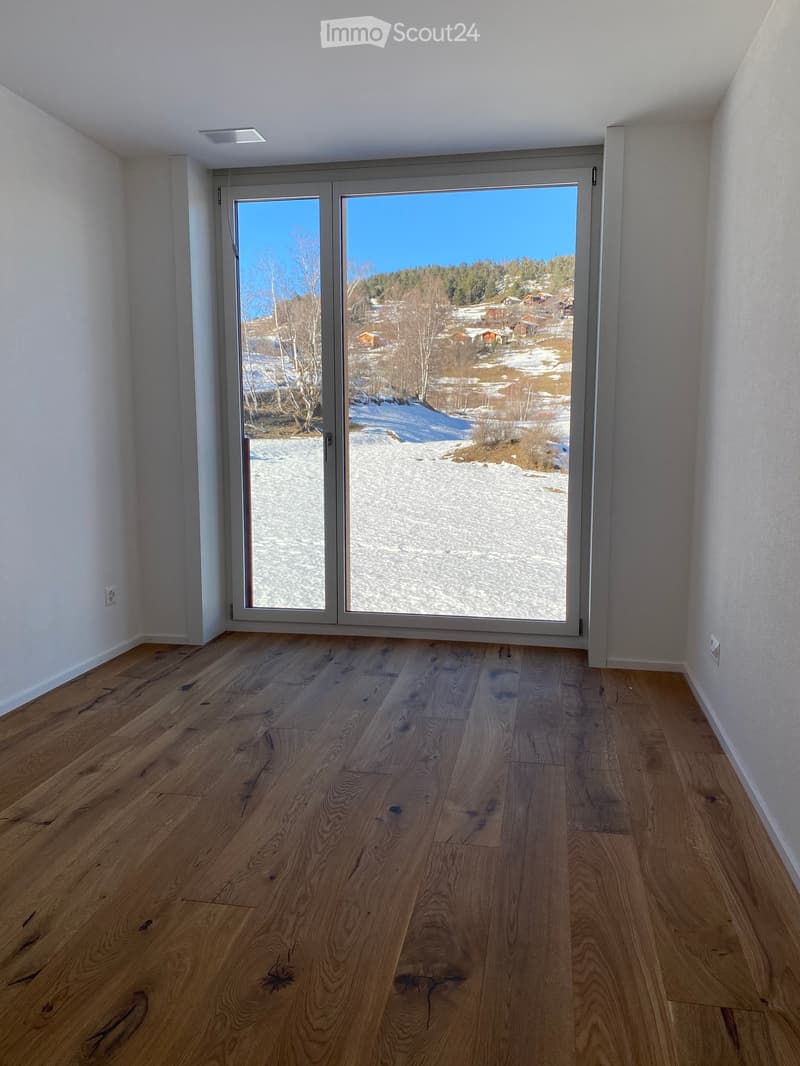 Empty room with wooden flooring and large sliding glass doors leading to a snowy outdoor view.