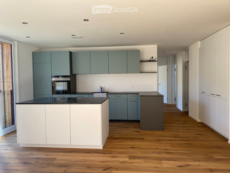 Modern kitchen with light blue and white cabinets, a central island with a black countertop, and wooden flooring.