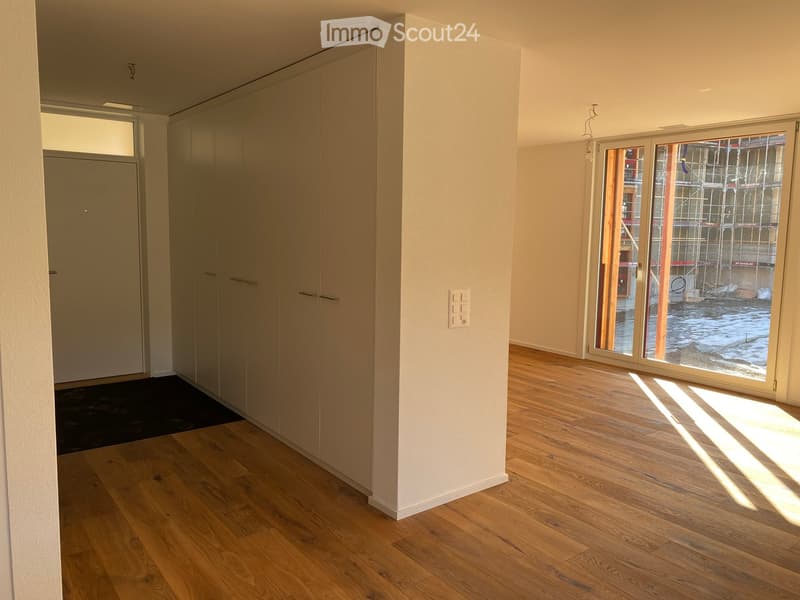 Empty room with light wooden flooring, white walls, built-in closet, and large window with view of construction site.