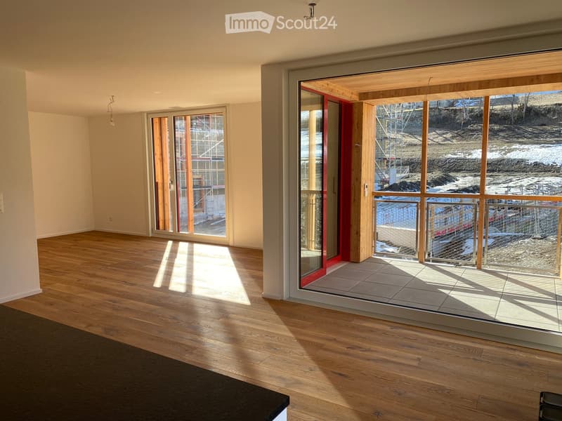 Empty room with wooden flooring, large glass sliding doors leading to a balcony, and natural light streaming in.