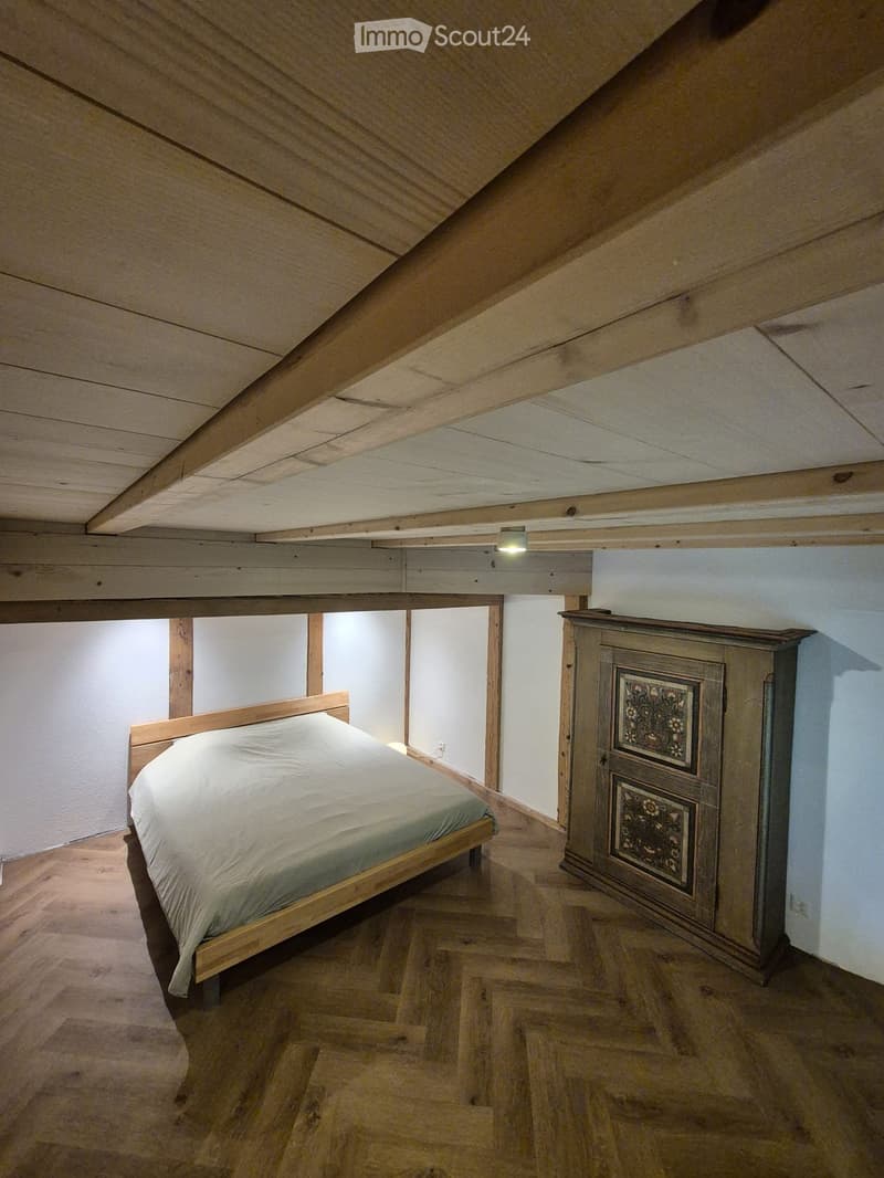 Cozy attic bedroom with wooden slanted ceilings, a single bed with white bedding, and a tall wooden wardrobe with decorative panels.