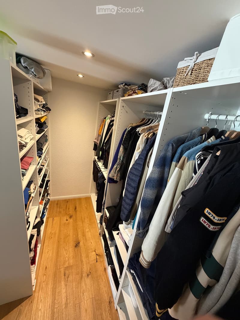 A well-organized walk-in closet with wooden flooring, white built-in shelving units, and various clothing items neatly arranged on hangers and shelves.