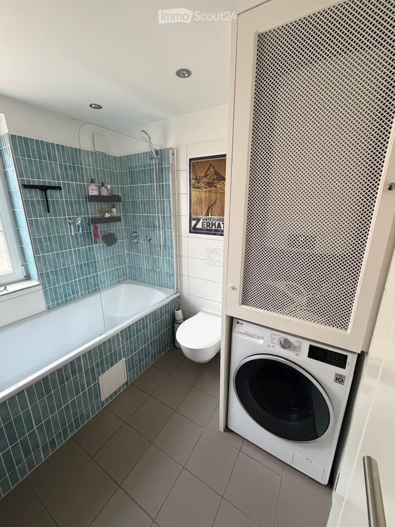 Modern bathroom with a bathtub, toilet, washing machine, and shower area with blue tiles.