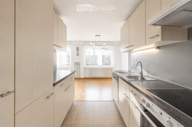 Modern kitchen with light wood cabinets, stainless steel appliances, and a sleek countertop. Features a sink, stove, and oven, with a chandelier hanging from the ceiling.