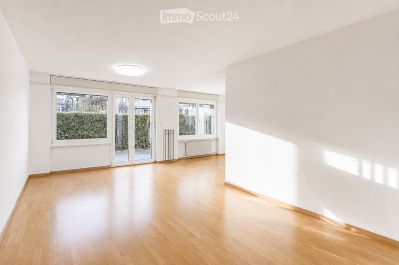Empty room with wooden flooring, white walls, large windows, and a sliding glass door leading to an outdoor area.
