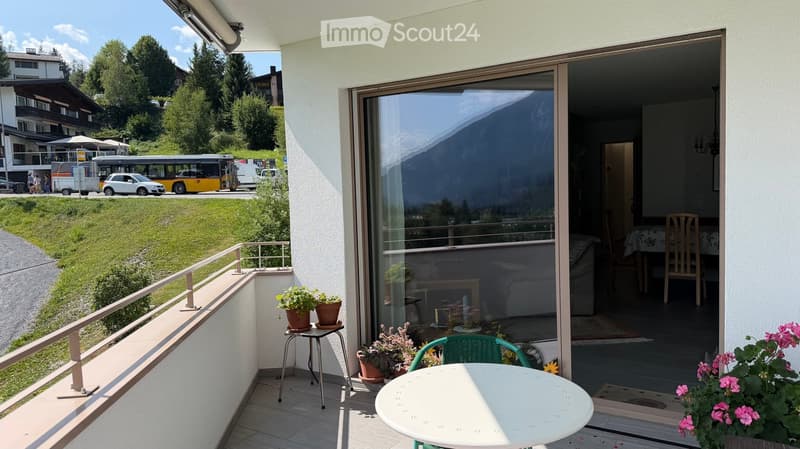 Balcony with a view of the mountains, featuring a white table, green chair, small stool, and potted plants.