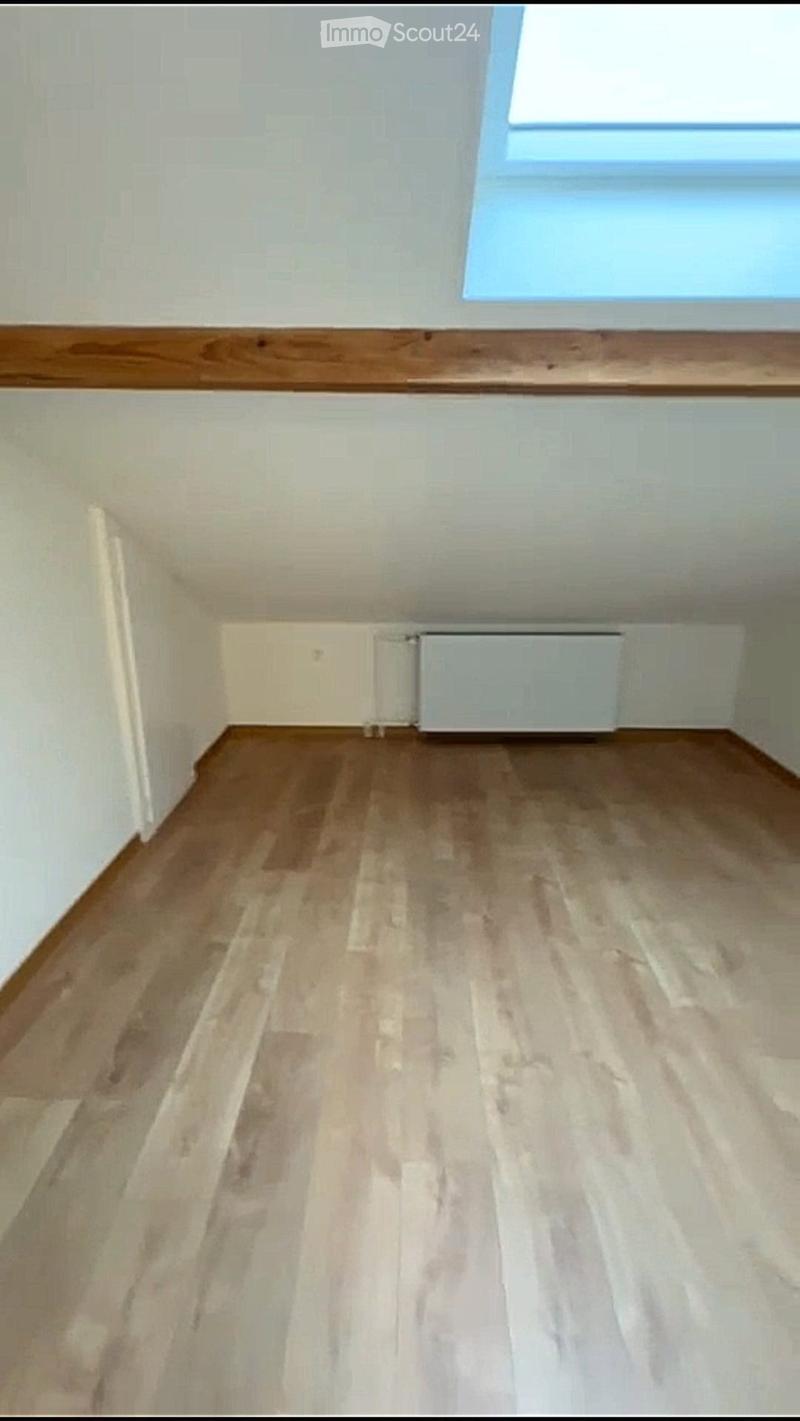 empty room with wooden floor and white walls, a white heater mounted on the wall, and a skylight