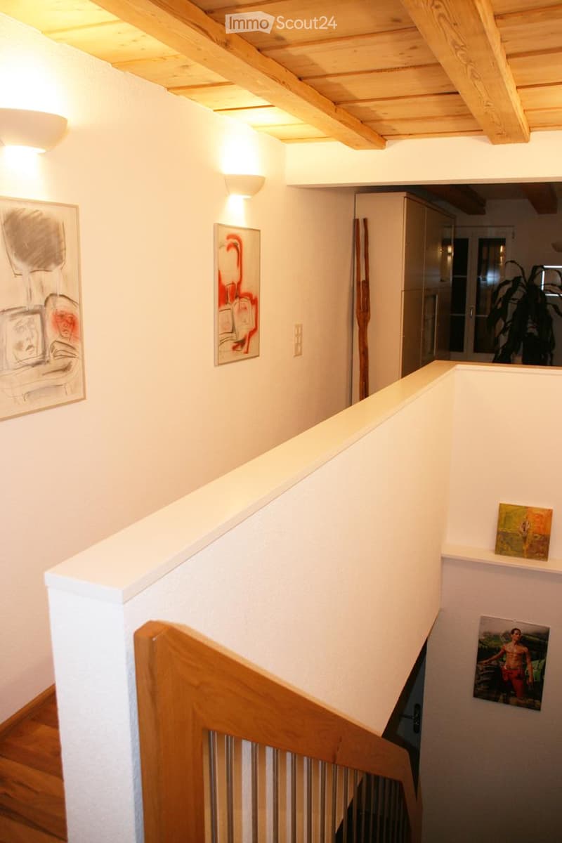 Staircase with wooden railings and white walls, decorated with framed artwork and modern lighting fixtures.