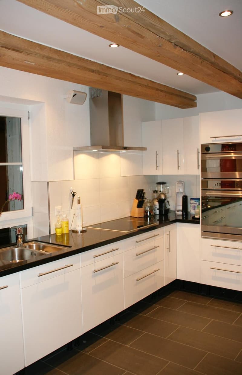 Modern kitchen with white cabinets, stainless steel appliances, and a black countertop. Features include a sink, oven, blender, coffee maker, and various kitchen accessories.