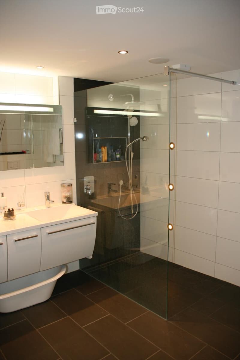 Modern bathroom with a white sink, large mirror, bathtub, glass-enclosed shower, and dark tiled floor.