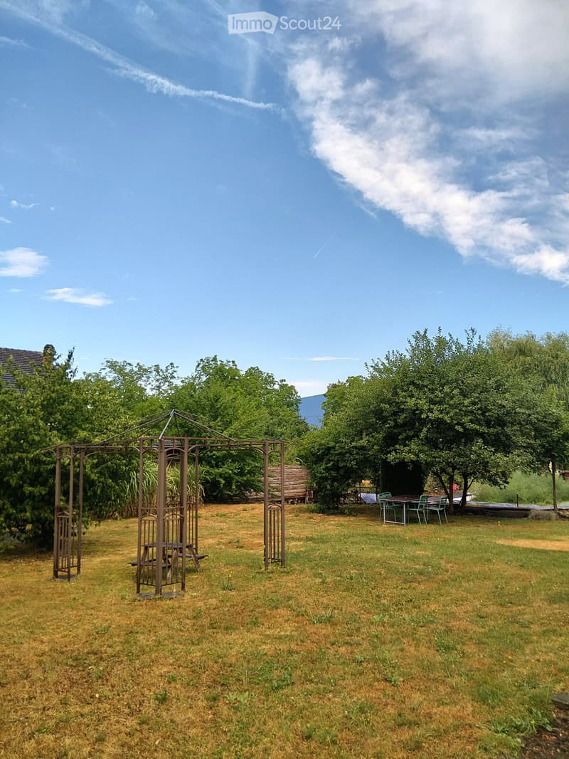A spacious garden with a metal gazebo, picnic table, and outdoor dining set under trees.