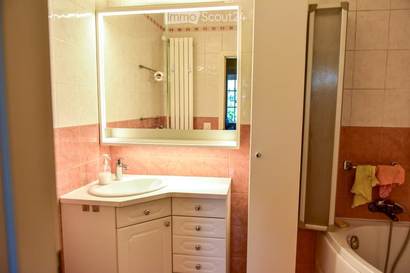 Bathroom with pink tiles, white countertop, sink, cabinet, mirror, shower area, bathtub