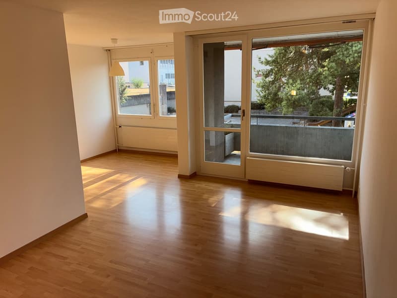 Empty room with wooden flooring, large windows, and a sliding glass door leading to a balcony area.