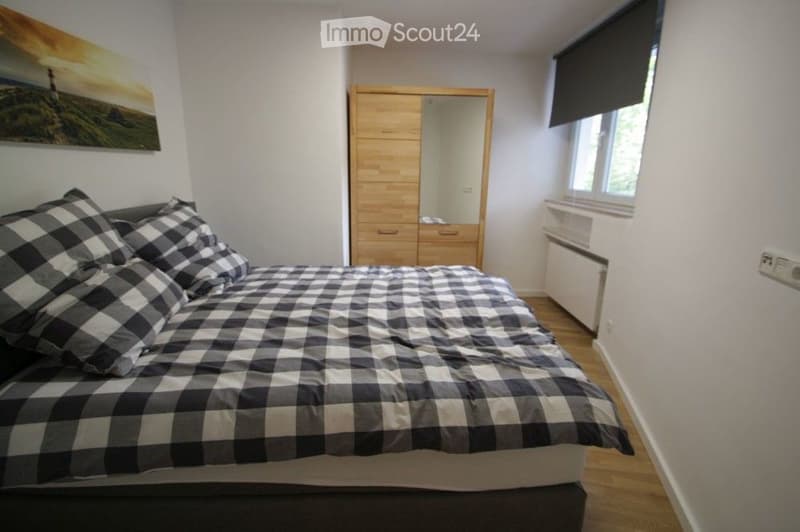 Cozy bedroom with a wooden bed, checkered bedding, a wooden wardrobe with a mirror, and a landscape painting on the wall.