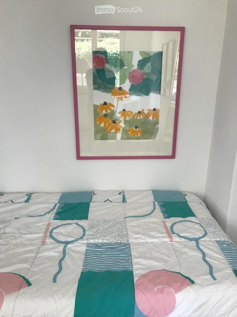A bedroom with a colorful patchwork quilt on the bed and a framed mirror on the wall.