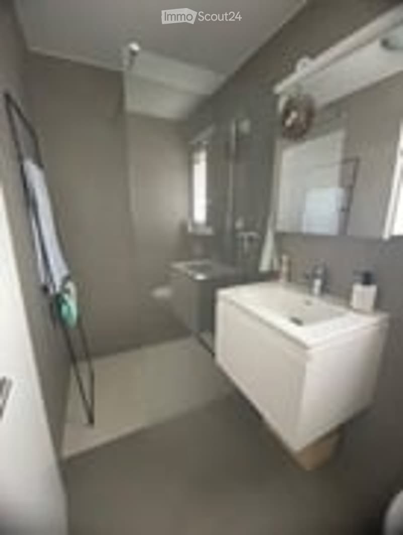 Modern bathroom with a white sink, bathtub, and large mirror. The walls are tiled in a neutral color, and the floor is covered with dark tiles.
