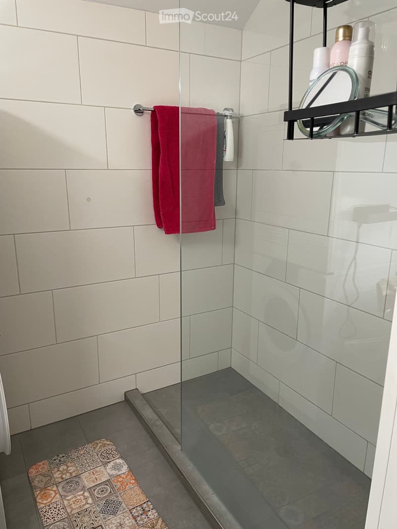 Modern bathroom with white tiled walls, glass shower enclosure, towel rack, and decorative bench outside the shower area.
