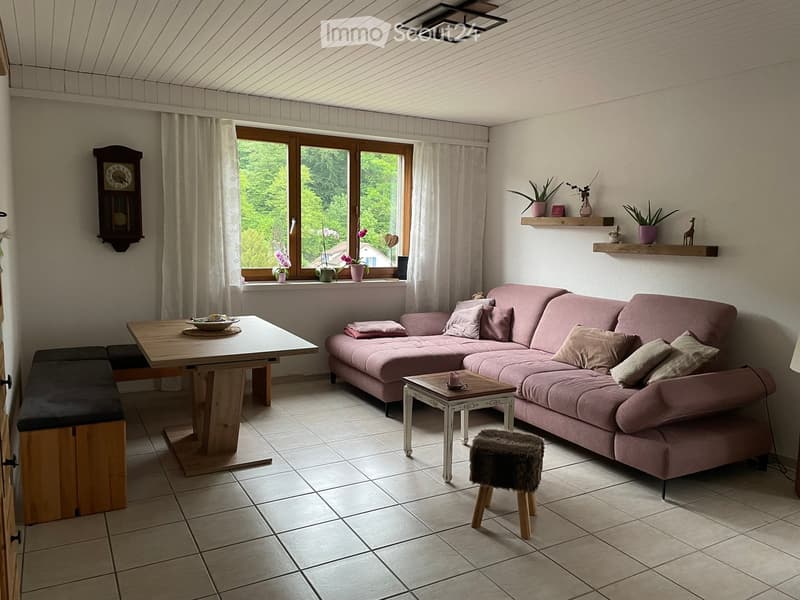 Living room with a pink sectional sofa, wooden coffee table, small round table, bench, and decorative shelves with vases and plants.