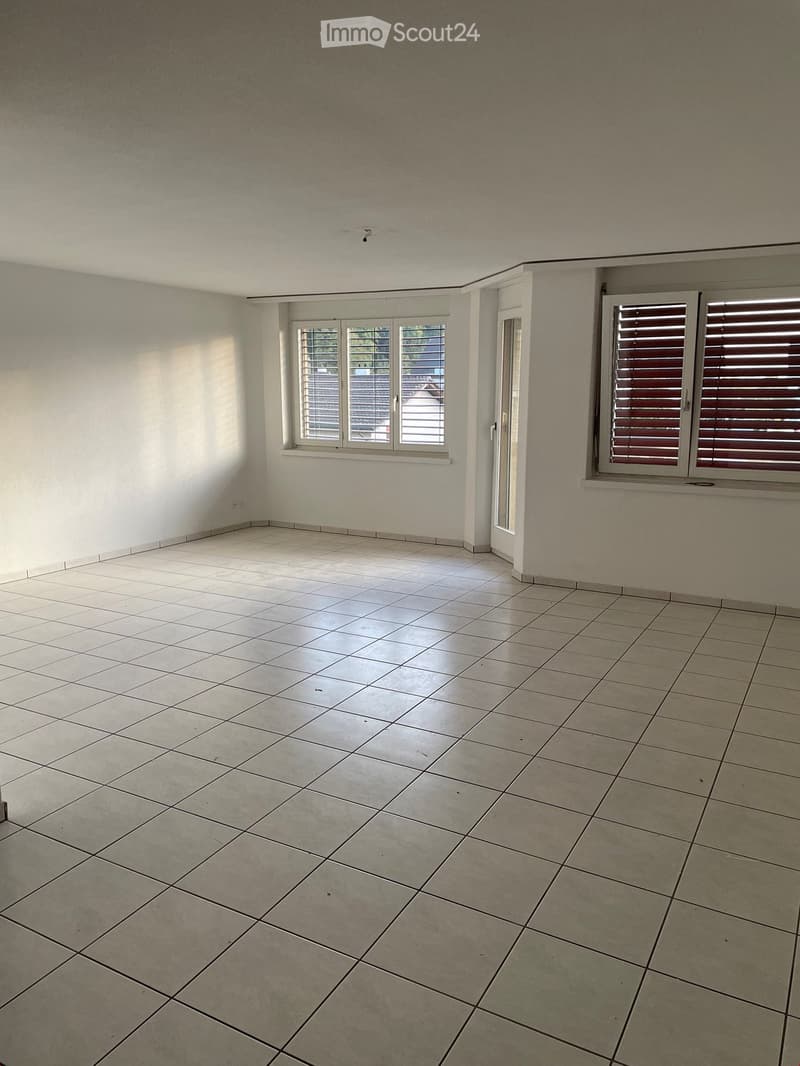 Empty room with tiled floor and white walls, featuring two windows and a door leading outside.