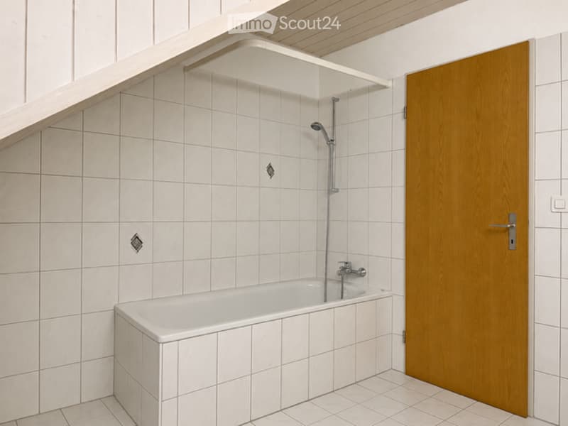 Modern bathroom with white tiled walls and floor, a bathtub, a showerhead, and a wooden door.