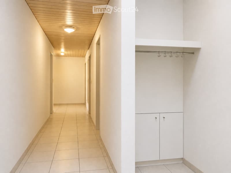 A clean, well-lit hallway with tiled flooring and white walls, featuring a built-in closet with white cabinetry and a coat rack.