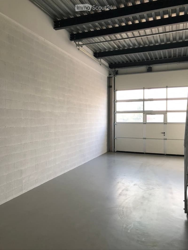 Empty garage with concrete floor, white brick walls, large overhead door, and exposed metal ceiling beams.
