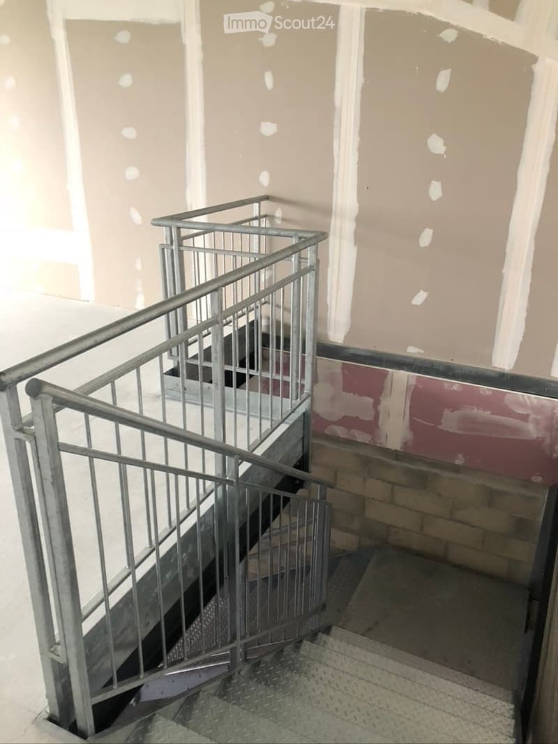 Staircase with metal railings, unfinished walls with visible patches of plaster and exposed brickwork, and a metal tread pattern on the stairs.