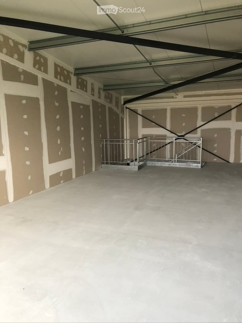 Empty room with bare walls and concrete floor, featuring exposed metal beams on the ceiling and a small metal staircase leading to an upper level.