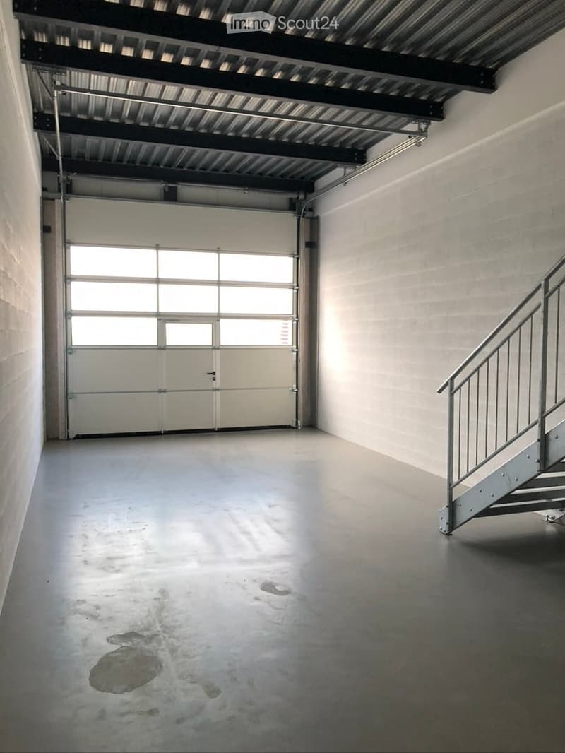 Empty garage with a large roll-up door, metal staircase leading upwards, and a concrete floor.