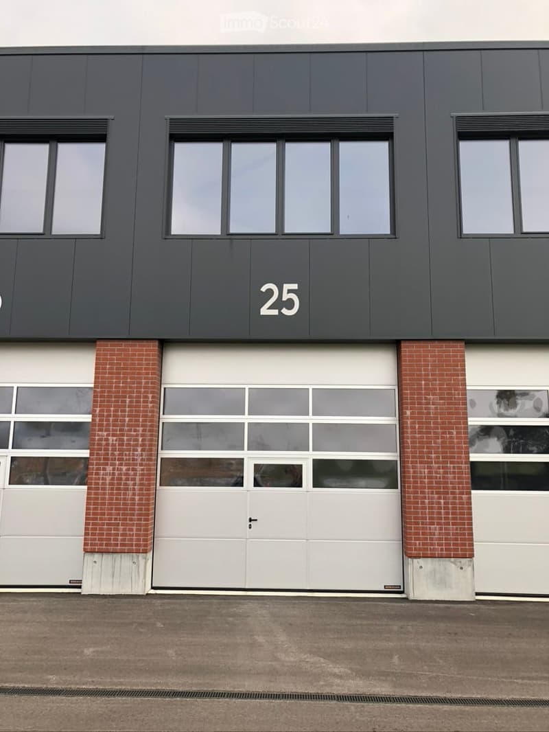 Modern industrial-style building with a large garage door, brick columns, and numbered '25' on the facade.