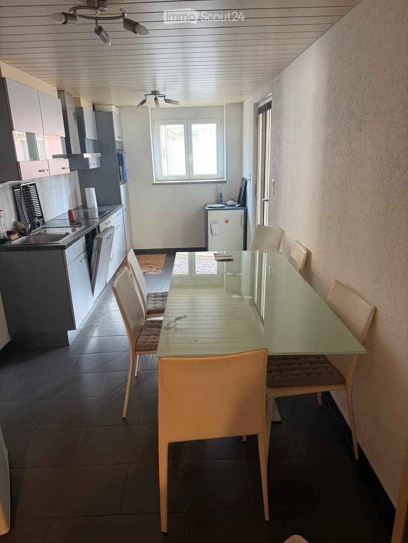 Open-plan kitchen and dining area with modern cabinets, a glass dining table with chairs, and a small refrigerator.