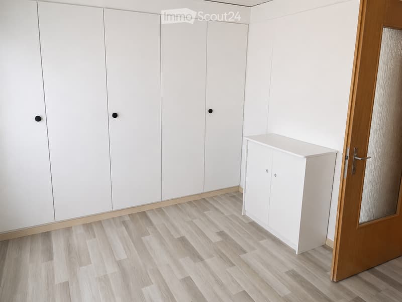 Empty room with white built-in wardrobes, light wooden flooring, and a small white console table near the door.