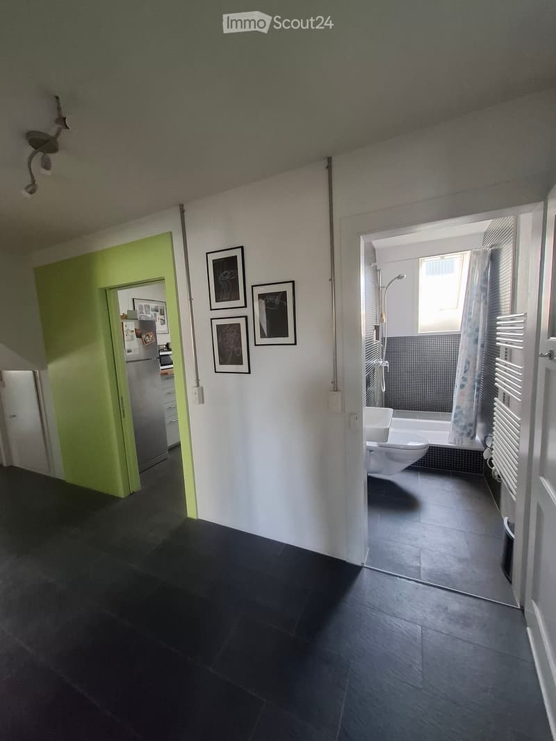 Modern bathroom with a toilet, sink, and shower area. The room features dark tiled flooring, white walls, and framed artwork on display.