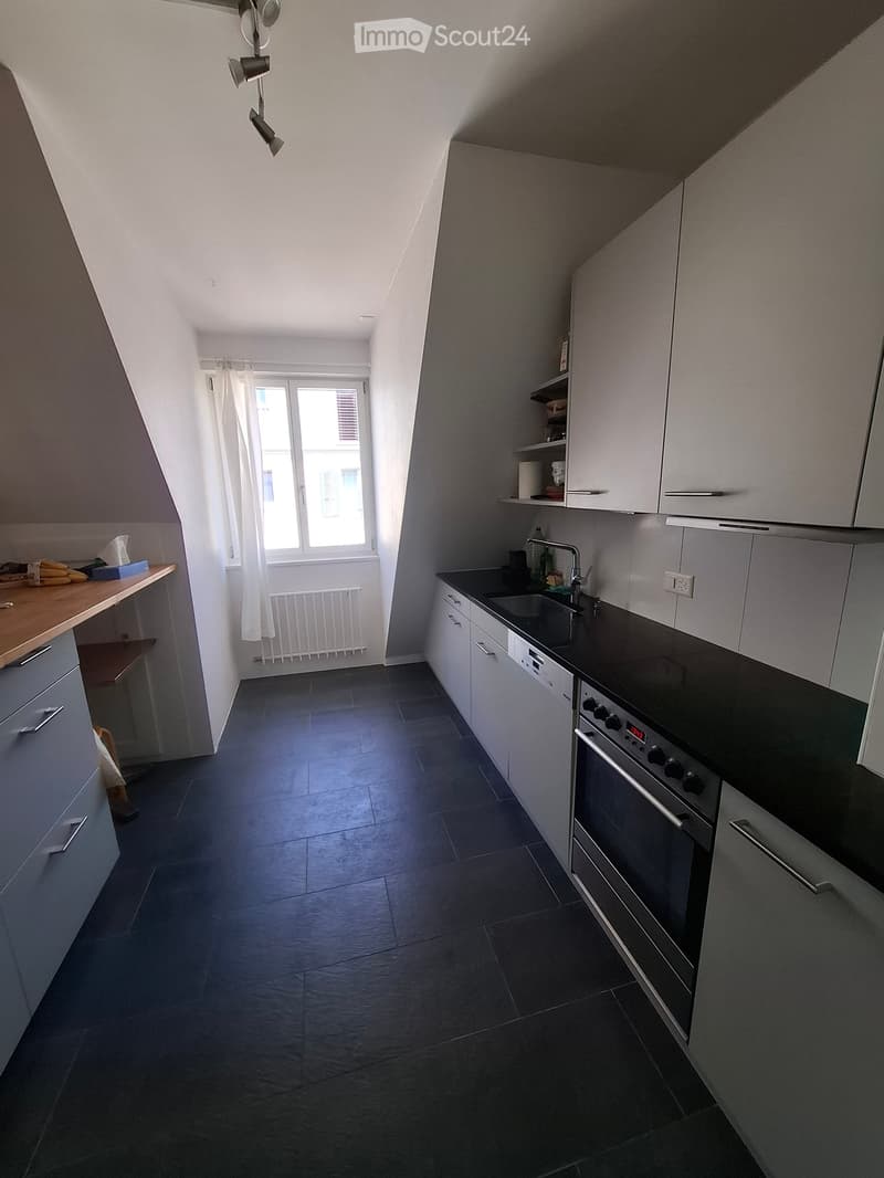 Modern kitchen with dark tiled floor, white cabinets, black countertop, sink, oven, and a window with white curtains.