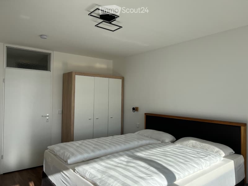 Modern bedroom with a double bed, white bedding, a built-in wardrobe, and sleek ceiling lights.