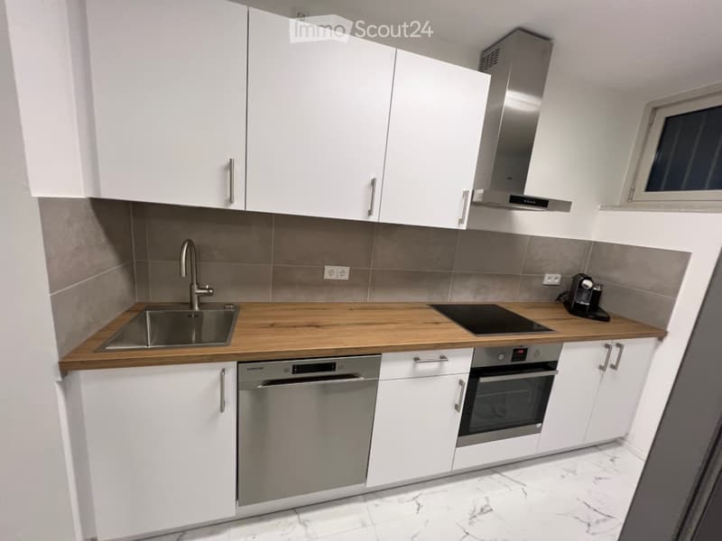 Modern kitchen with white cabinets, wooden countertop, stainless steel appliances including a sink, stove, oven, and dishwasher, and a range hood above the stove.
