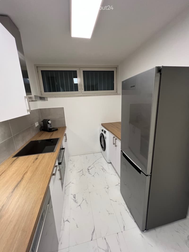 Modern kitchen with marble flooring, wooden countertops, stainless steel appliances including a refrigerator, washing machine, and coffee maker, and an induction cooktop.