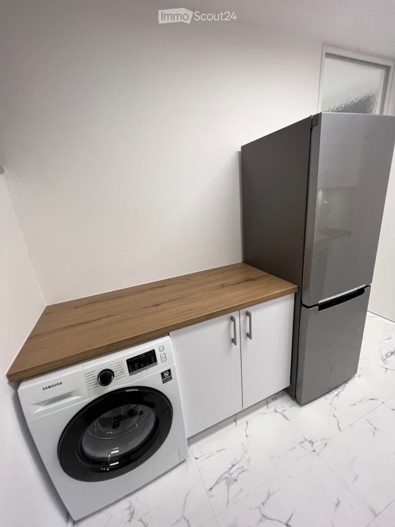 Modern bathroom with a white washing machine, a refrigerator, and white cabinets with a wooden countertop.
