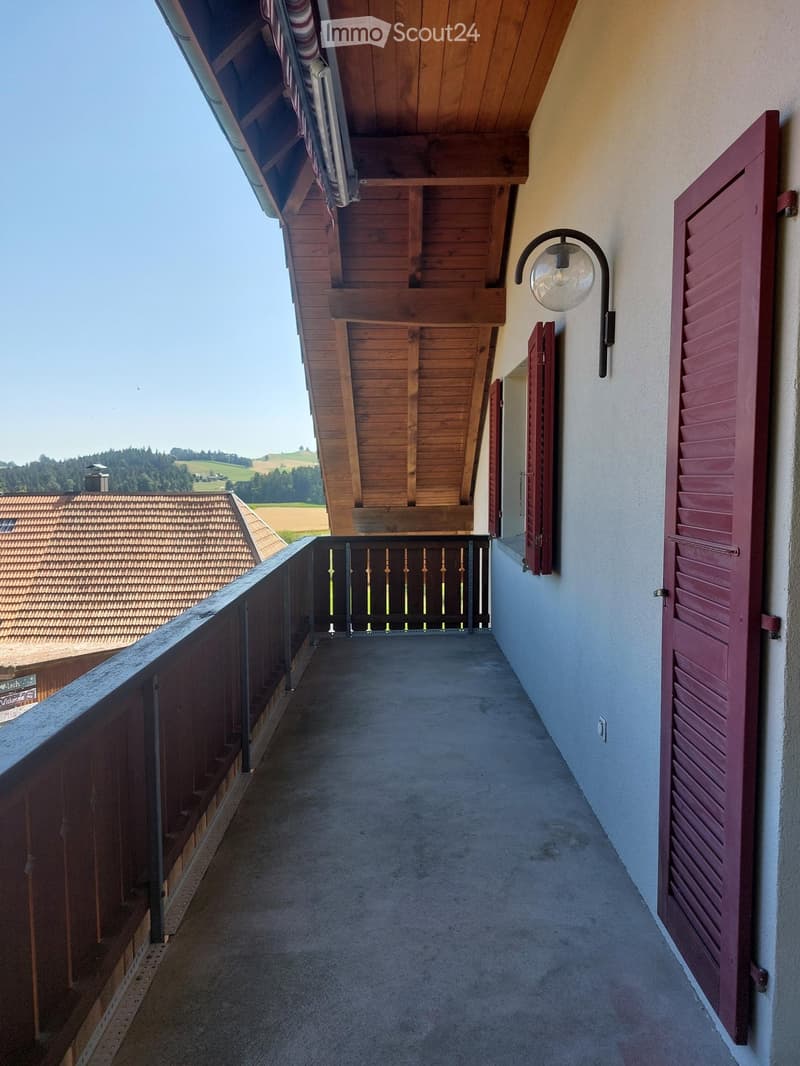 Balcony with wooden railing, concrete floor, and wooden shutters on the wall.