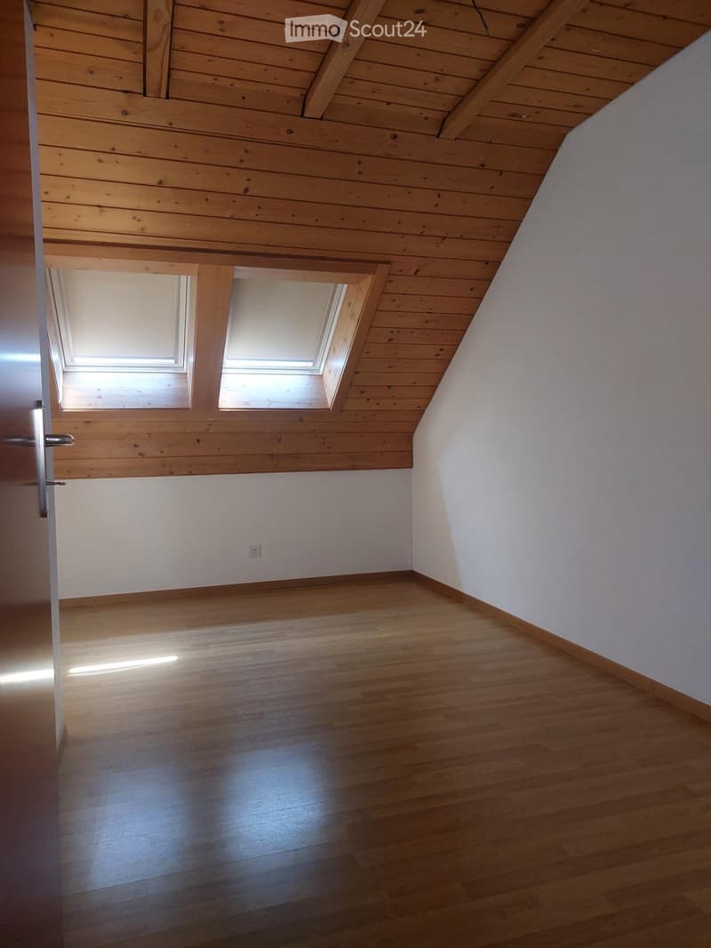Empty attic room with wooden floors and slanted wooden ceilings, featuring two skylight windows and white walls.
