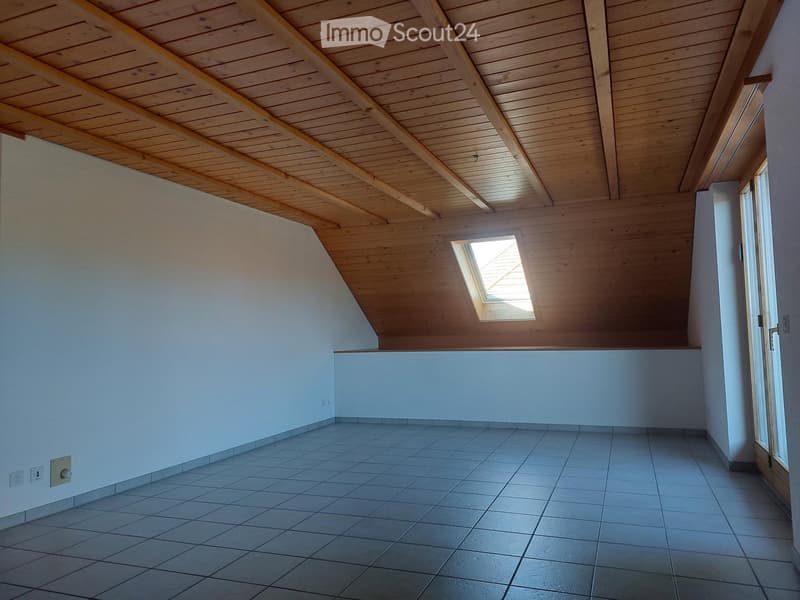 Empty room with wooden slanted ceiling, tiled floor, white walls, and a skylight window bringing in natural light.