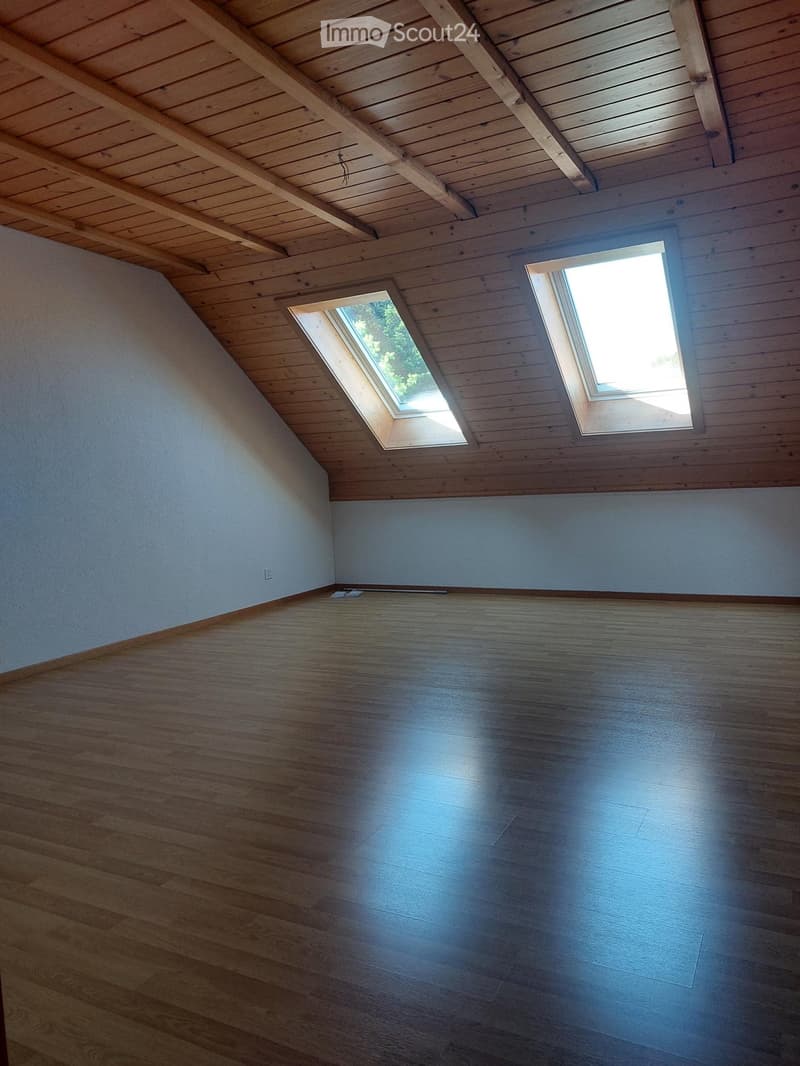 Empty attic room with wooden floors and exposed wooden beams, featuring two skylights allowing natural light to enter.