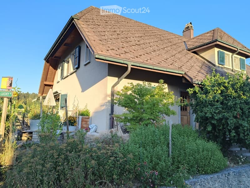 Two-story house with a tiled roof, multiple windows, and a well-maintained garden with various plants and flowers.
