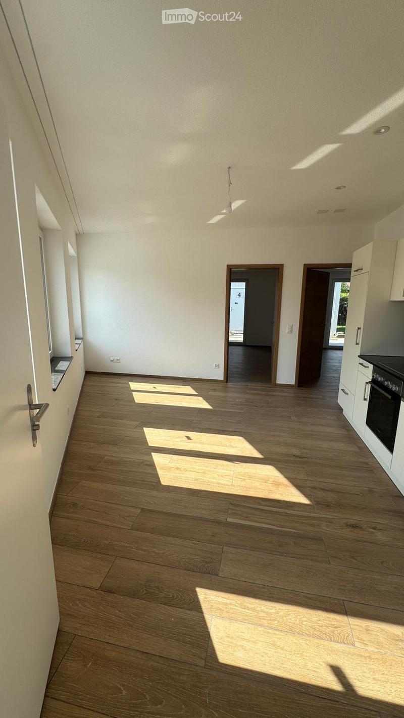 Empty room with wooden flooring and white walls, featuring natural light from windows and a door leading to another room.
