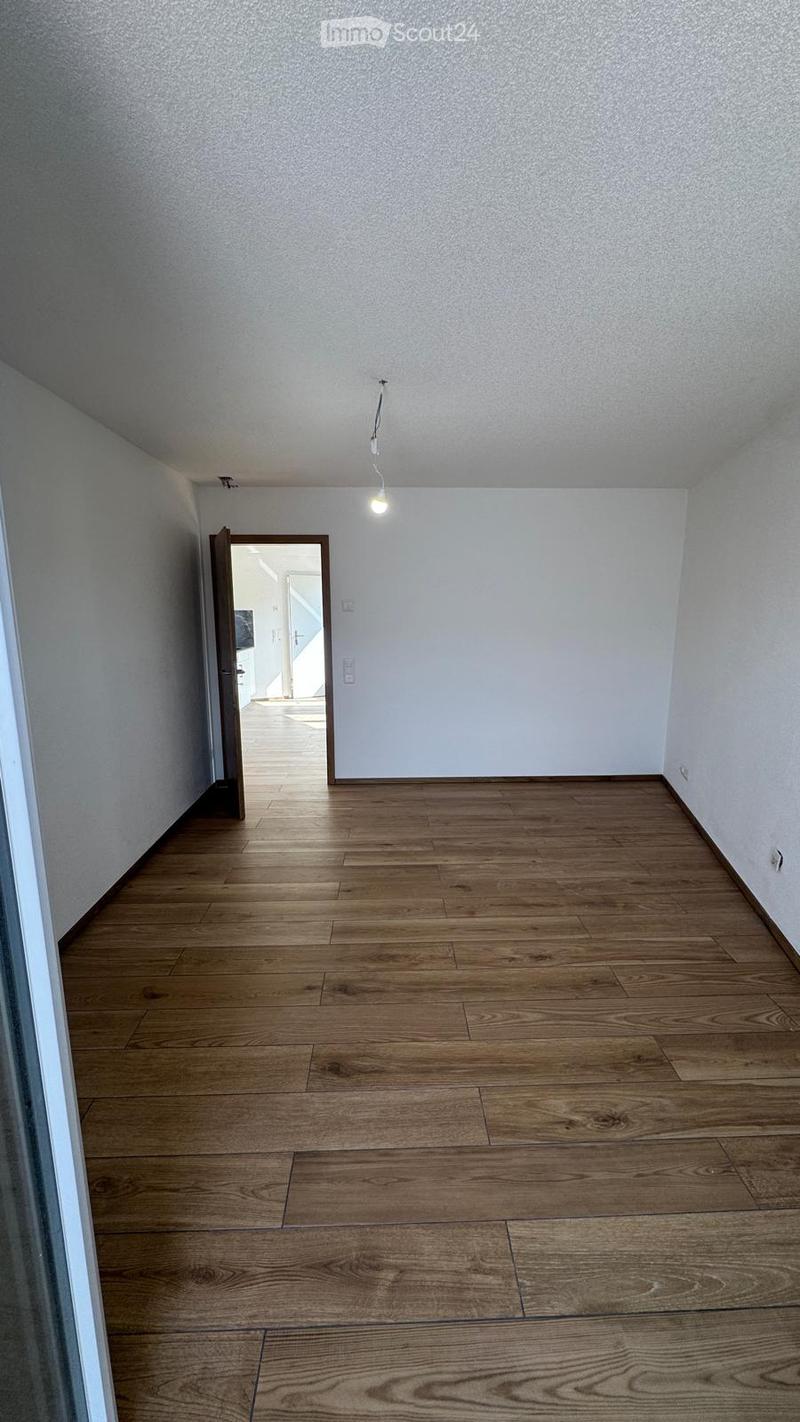 Empty room with wooden flooring and white walls, featuring a single light fixture and an open doorway leading to another space.