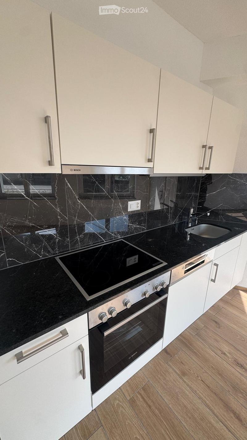 Modern kitchen with white cabinets, black marble countertops, stainless steel appliances including an oven, induction cooktop, and sink.