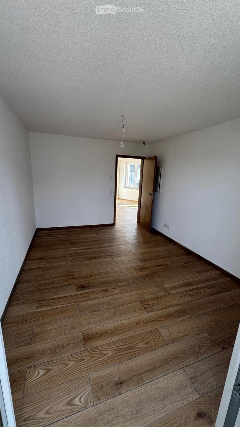 Empty room with wooden flooring and white walls, featuring a single light fixture and an open doorway leading to another room.